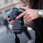 A woman adjusting a DSLR camera outdoors, focusing on her hands and device. Perfect for photography themes.