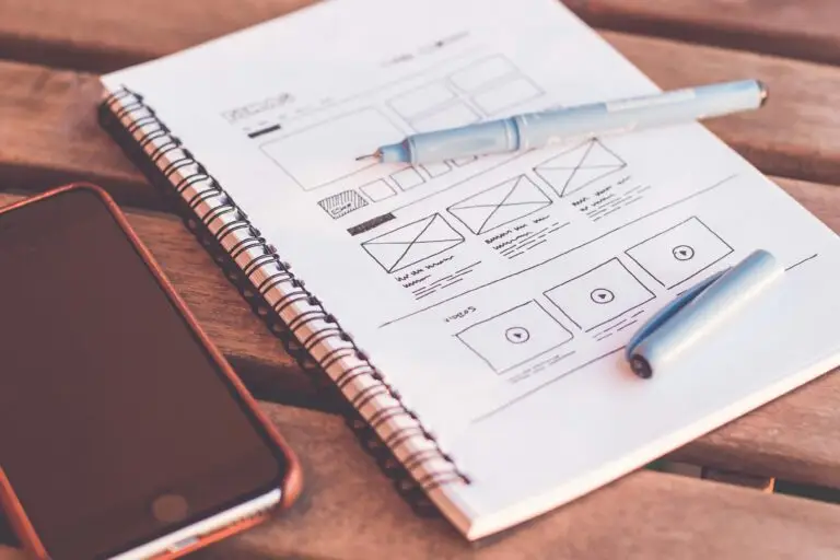 Close-up of a notebook with wireframe sketches and a smartphone on a wooden desk.