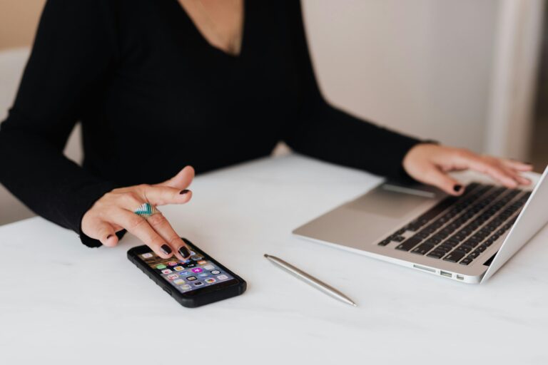 A professional woman multitasking with a smartphone and laptop at an office desk.