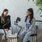 Diverse women communicating while recording voice in studio with white brick walls in daytime